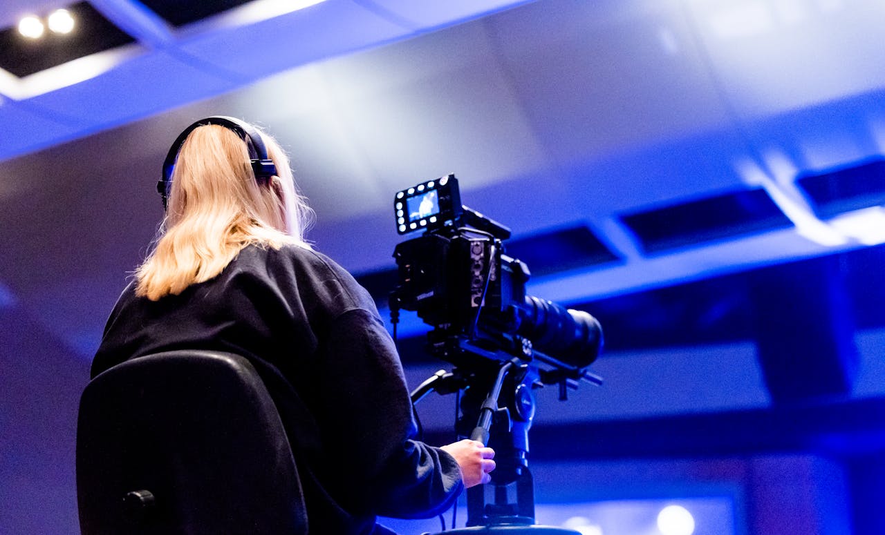 Blonde videographer with professional camera and headphones filming indoors.