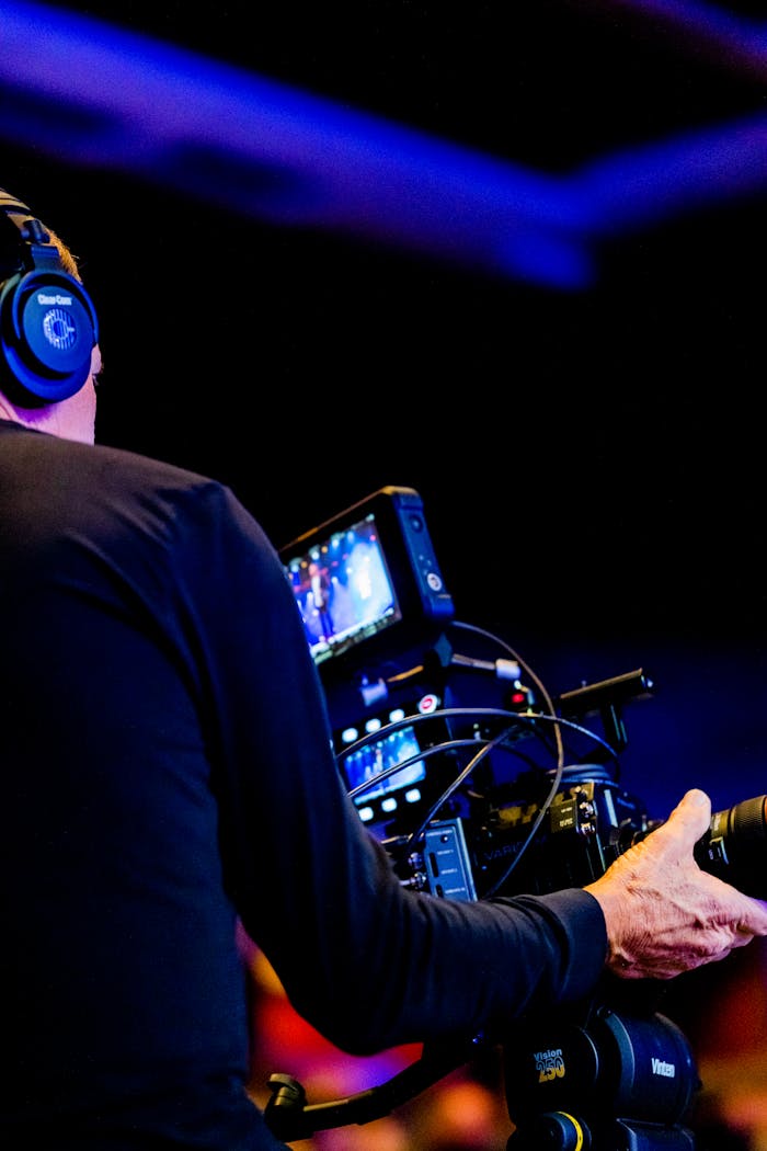 Cameraman using professional equipment to film in a dimly lit studio setting.