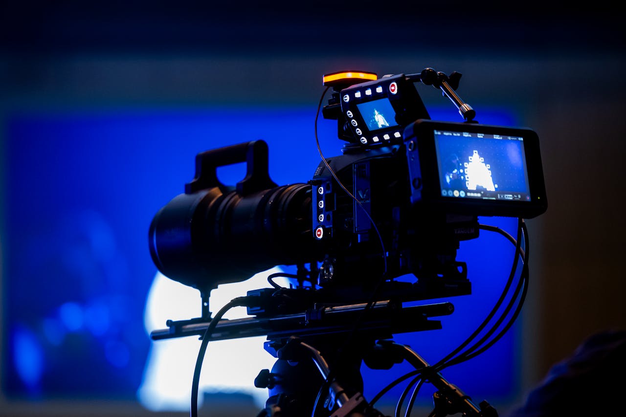 High-end video camera rig in studio setting with auxiliary monitor displays and vibrant blue lighting.